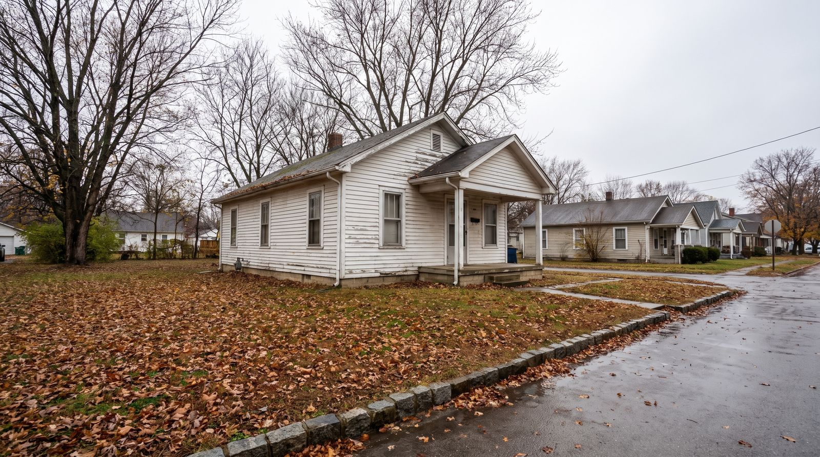 A modest white clapboard house with a small front porch on an ordinary residential corner in autumn