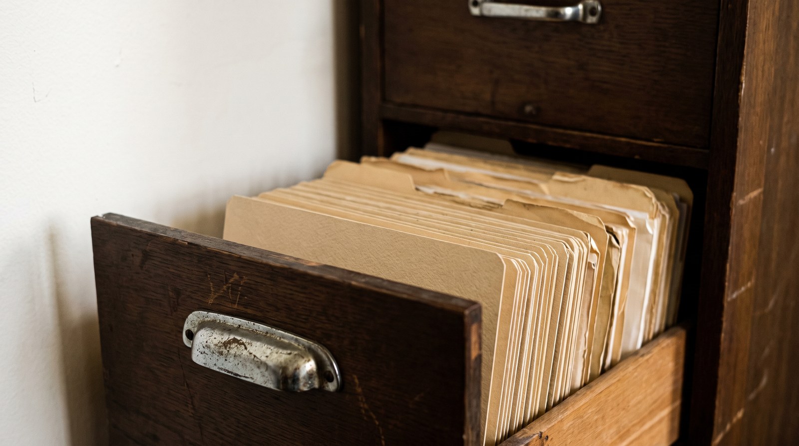 An old wooden filing cabinet with one drawer pulled open showing plain unlabelled card dividers and manila folders