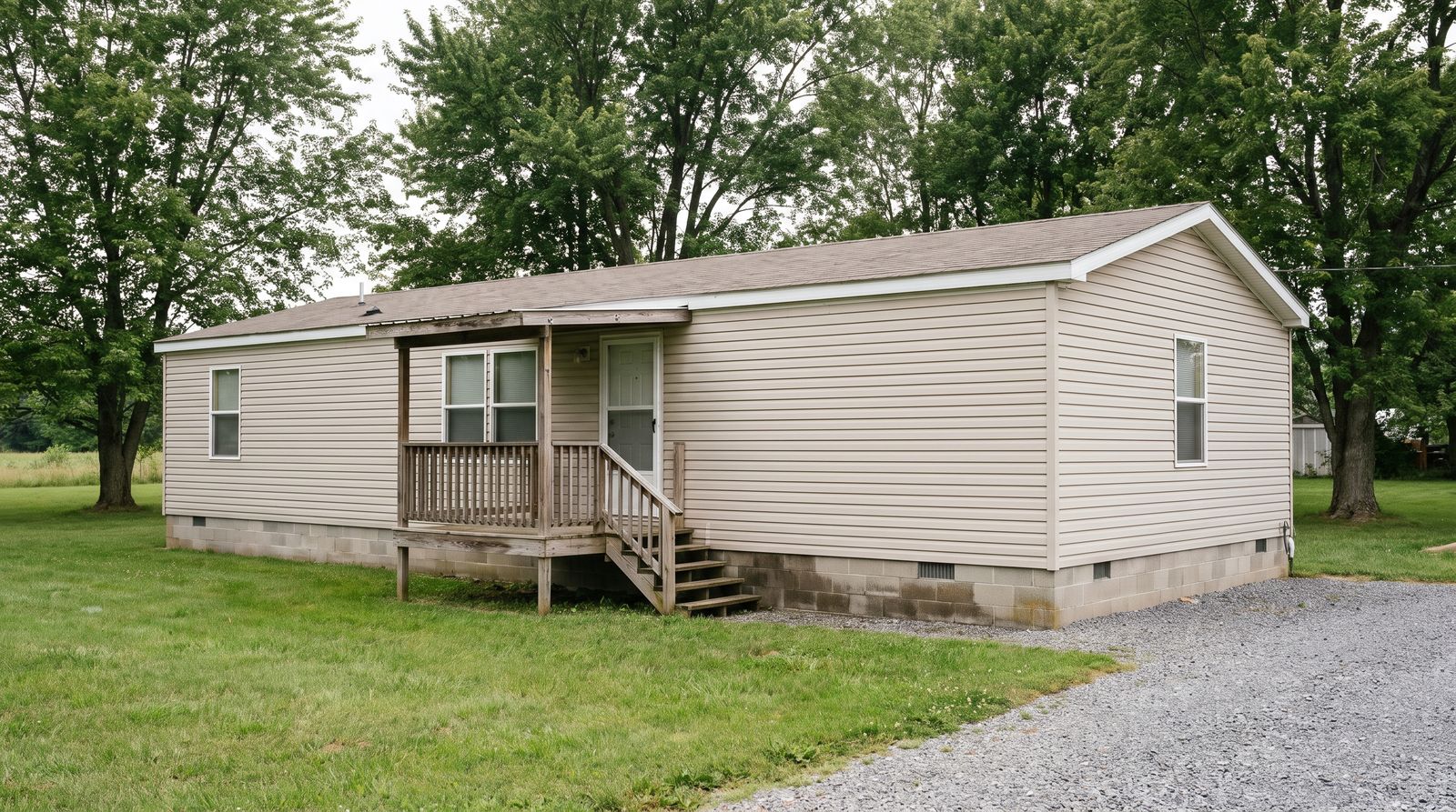 A single-wide manufactured home on its own grassed lot with a small covered porch and masonry skirting along the base
