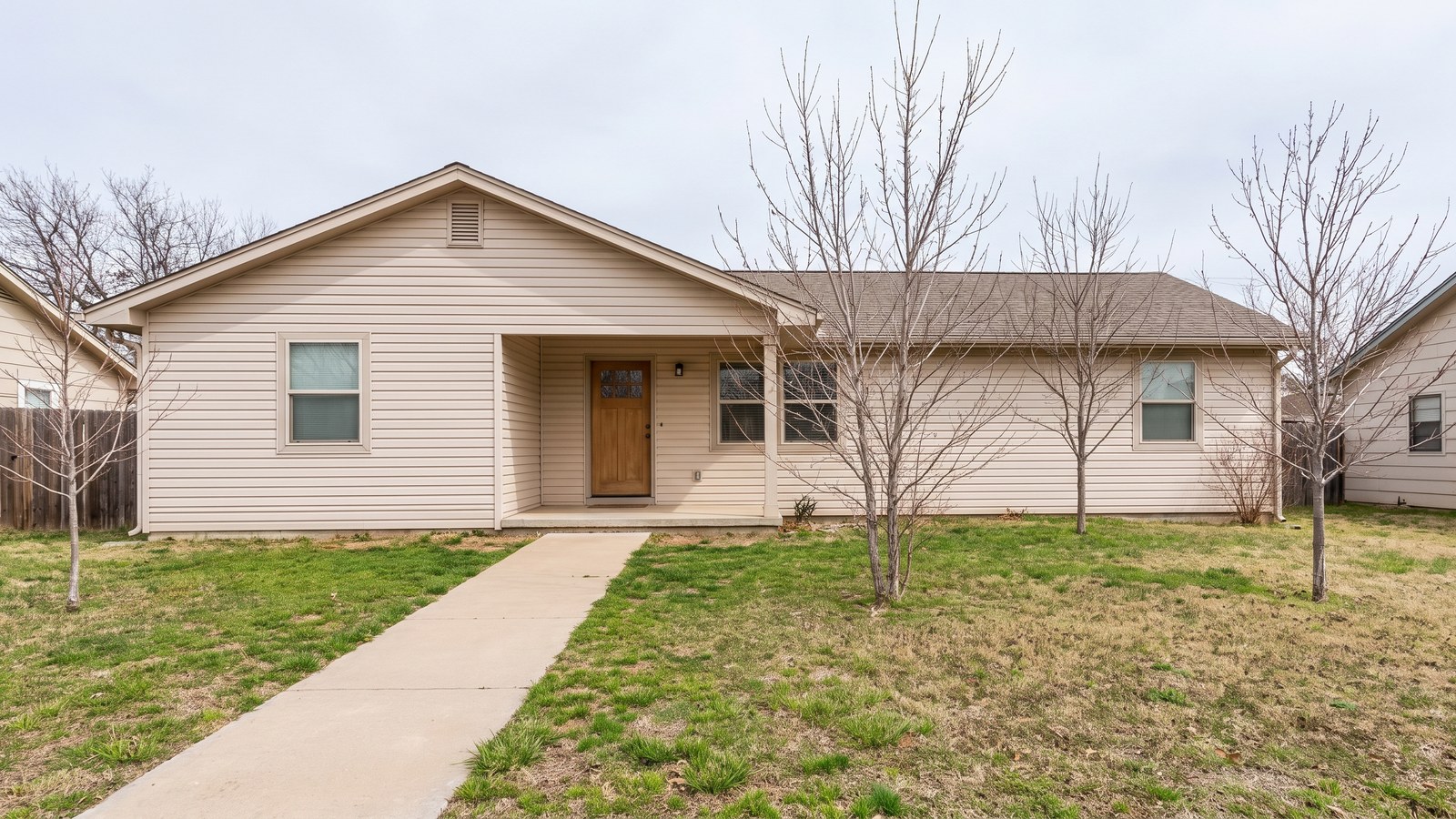 The exterior of a modest well-kept single-storey house in early spring with a tidy front lawn and a simple concrete path to the front step