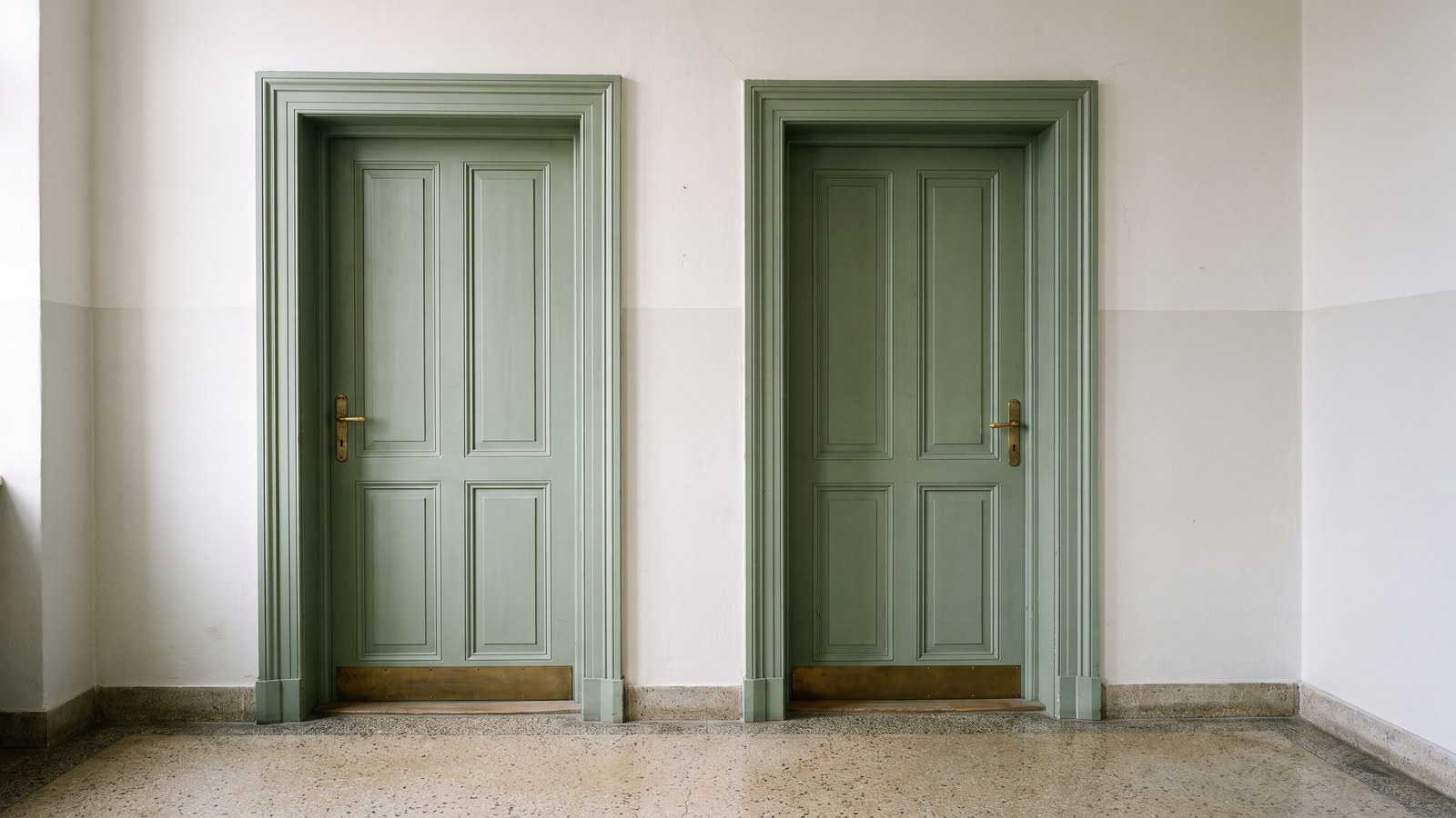 Two identical plain closed doors side by side in a quiet institutional corridor